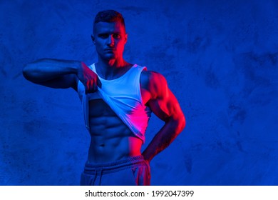 Handsome bodybuilder showing his abdominal muscles in colorful neon light