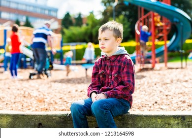 A handsome boy with ADHD, Autism, Asperger Syndrome sitting at the park, scared and apprehensive about playing with the other children, looking nervous and worried - Shutterstock ID 1213164598