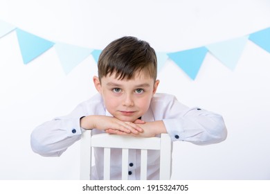 handsome boy from elementary school posing while sitting on a chair against a background of blue flags