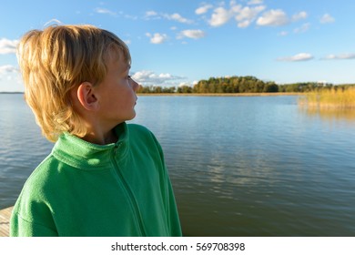 Handsome boy thinking while looking back on wooden pier against scenic view of blue sky and river