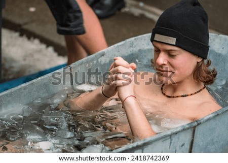 Handsome boy wearing a hat ice bathing in the cold water among ice cubes in a vintage bathtub. Wim Hof Method, cold therapy, breathing techniques, yoga and meditation