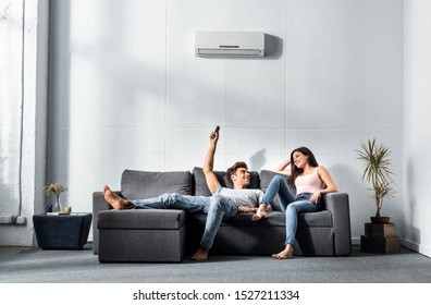 handsome boyfriend switching on air conditioner and looking at smiling girlfriend