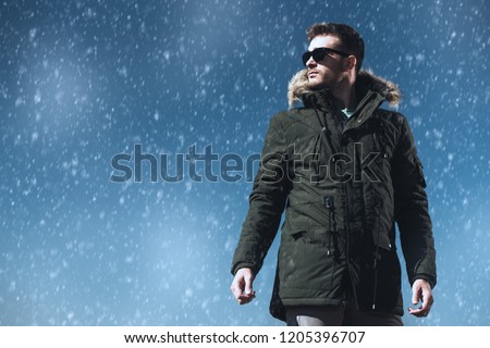 A handsome brutal man wearing a parka and sunglasses. Fashion for men. Autumn, winter.
