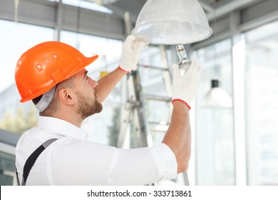 Handsome builder is screwing an electric light bulb into a fixture. He is standing and looking up with concentration - Powered by Shutterstock