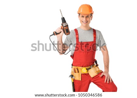 Handsome builder in uniform with tool belt holding drill isolated on white