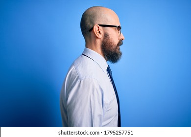 Handsome business bald man with beard wearing elegant tie and glasses over blue background looking to side, relax profile pose with natural face with confident smile.