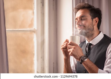 Handsome Business Man Enjoying His Morning Cup Of Coffee, Getting Ready For Work, Enjoying City View From A Window