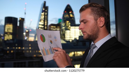 Handsome Business Man Examining Pie Chart Sales Data Profits At Window With London City Skyline In Background