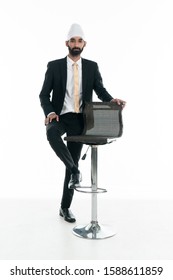 Handsome Business Man In Suit And Tie Presenting A Bar Chair Or Stool. Successful Businessman Standing Beside A High Bar Chair.