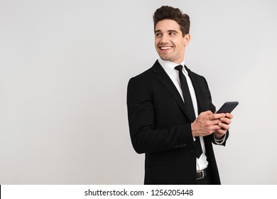 Handsome Business Man Wearing Suit Standing Isolated Over Gray Background, Using Mobile Phone