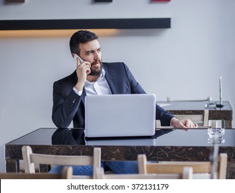 Handsome Business Man Working On His Lap Top In Restaurant.Young Business Man Talking On The Phone, And Smiling,shallow Depth Of Field