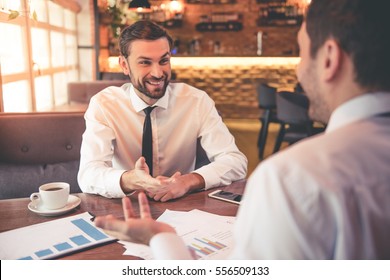 Handsome business partners are discussing work and smiling while sitting in cafe