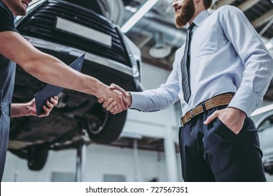 Handsome businessman and auto service mechanic are discussing the work and shaking hands. Car repair and maintenance. - Powered by Shutterstock