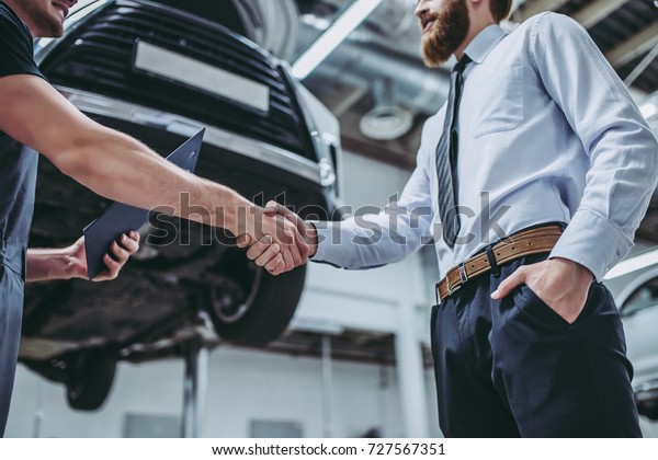 Handsome
businessman and auto service mechanic are discussing the work and
shaking hands. Car repair and
maintenance.