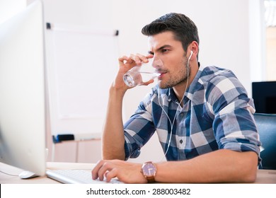 Handsome businessman in casual cloth using PC and drinking water in office