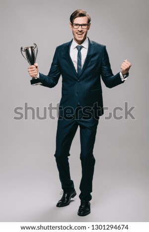 handsome businessman celebrating victory and holding trophy in hand on grey background 