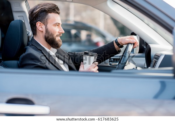 Handsome businessman driving a car with coffee to go\
in the city