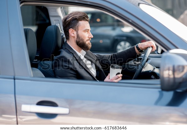 Handsome businessman driving a car with coffee to go
in the city