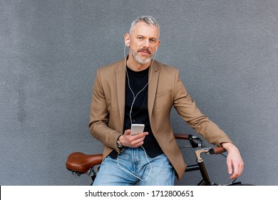 handsome businessman in earphones listening music while holding smartphone near bicycle outside - Powered by Shutterstock