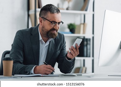 handsome businessman in formal wear holding smartphone and pen - Shutterstock ID 1513156076