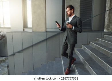 Handsome businessman goes down stairs with coffee and phone during break near office