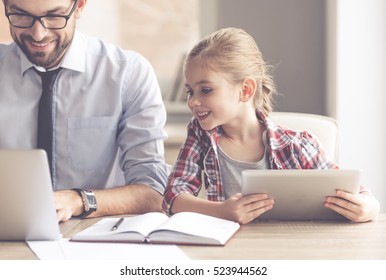 Handsome businessman and his cute little daughter are using gadgets and smiling while spending time together - Powered by Shutterstock