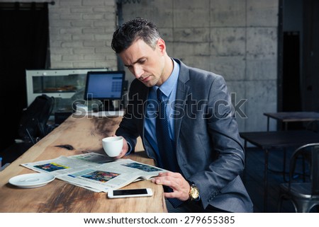 Handsome businessman reading magazine and drinking coffee in cafe