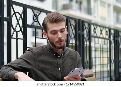 Handsome businessman sits on the bench and holds in hand white smartphone, looks photos - Shutterstock ID 1914559891