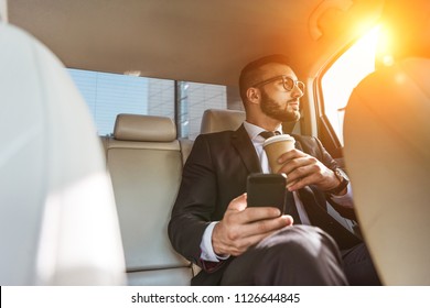 handsome businessman sitting in car with disposable coffee cup and smartphone - Powered by Shutterstock