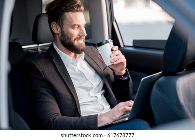 Handsome businessman sitting with coffee to go on the backseat of the car - Powered by Shutterstock