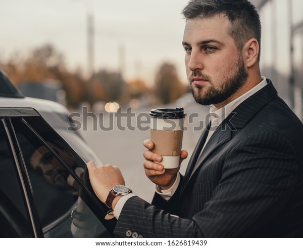Handsome businessman with smartphone near vehicle\
on office parking