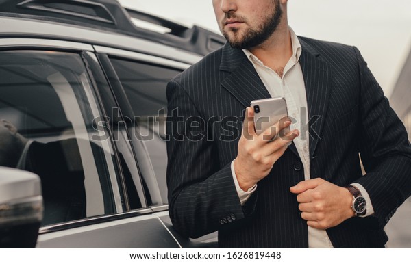 Handsome businessman with smartphone near vehicle\
on office parking