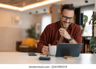 Handsome businessman smiling, using tablet and holding a cup of coffee. Photo of a male working on a tablet or reading news while drinking coffee. - Powered by Shutterstock