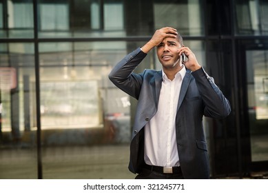 Handsome businessman standing at street, talking on a mobile phone and having bad conversation. 