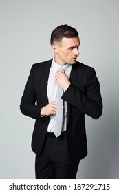 Handsome businessman straightening his tie on gray background