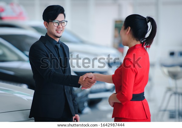 Handsome businessman in a suit enters into a\
car sale agreement with a saleswoman and shakes hands at a new car\
showroom.