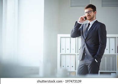 Handsome businessman in suit and eyeglasses speaking on the phone in office