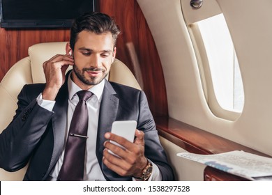 handsome businessman in suit listening music and using smartphone in private plane 