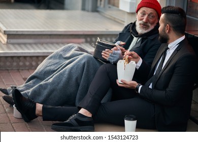 Handsome businessman in suit sitting on floor with homeless man together, listen to his story of life. Contrast people, rich and poor, but doesn't matter - Shutterstock ID 1543124723