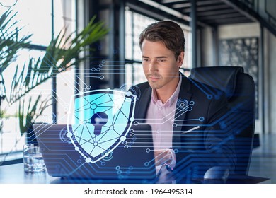 Handsome Businessman In Suit At Workplace Working With Laptop To Defend Customer Cyber Security. Concept Of Clients Information Protection And Brainstorm. Padlock Hologram Over Office Background.