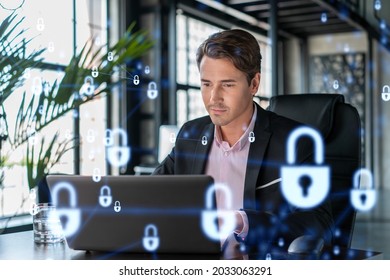 Handsome Businessman In Suit At Workplace Working With Laptop To Defend Customer Cyber Security. Concept Of Clients Information Protection And Brainstorm. Padlock Hologram Over Office Background.