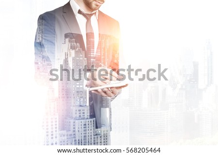 Handsome businessman in suit writing in notepad on creative city background with copy space. Young engineer taking notes. Double exposure