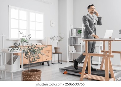 Handsome businessman talking by mobile phone on treadmill at table in office - Powered by Shutterstock