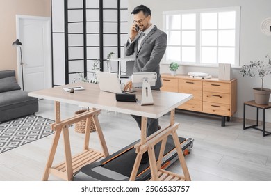 Handsome businessman talking by mobile phone on treadmill at table in office - Powered by Shutterstock