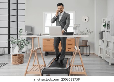 Handsome businessman talking by mobile phone on treadmill at table in office - Powered by Shutterstock