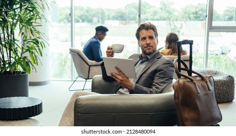 Handsome Businessman Using Digital Tablet And Drinking Coffee While Waiting For His Flight In The Airport VIP Lounge