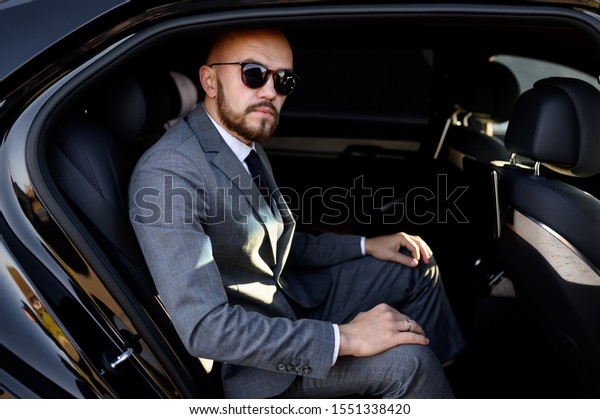 handsome businessman using his mobile phone in a modern\
car with a driver in center of the city. Concept of business,\
success, traveling, luxury\
