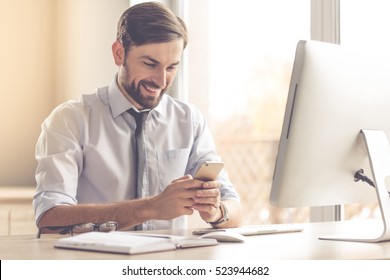 Handsome businessman is using a smartphone and smiling while working in office - Powered by Shutterstock