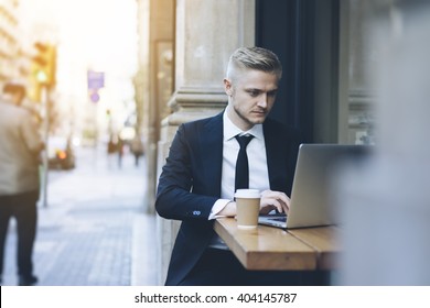 Handsome Businessman Wearing Suit And Using Modern Laptop Outdoors, Successful Manager Working In Cafe During Break And Searching Information In Internet On His Notebook Computer