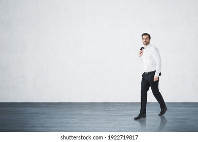 Handsome Businessman In White Shirt Holding His Jacket Is Walking Along Concrete Wall. Mockup. Concept Of Success In Career.